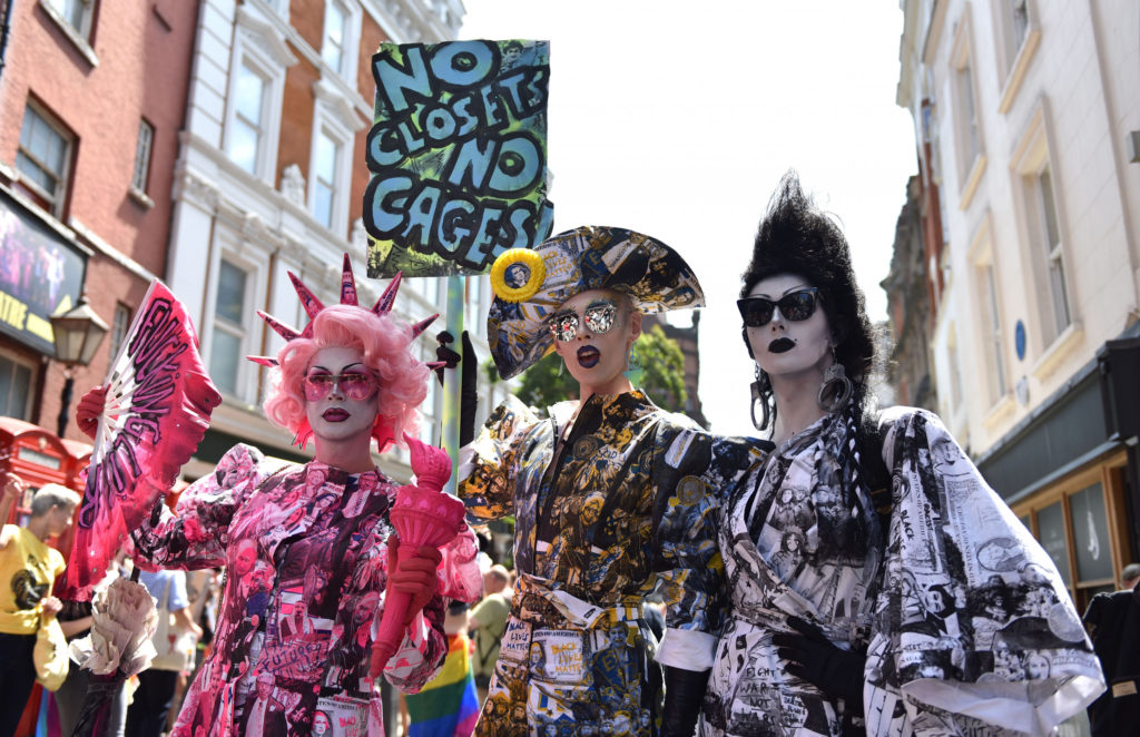 Tres drag queens protestando en las calles de new york una va vestida de rosa con una corona y una antorcha como la estatua de la libertad, pero rosada las otras dos van con trajes similares a piratas.